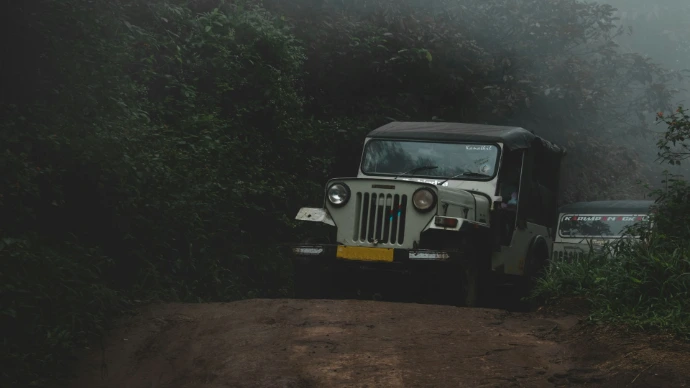 a jeep driving down a dirt road next to a forest